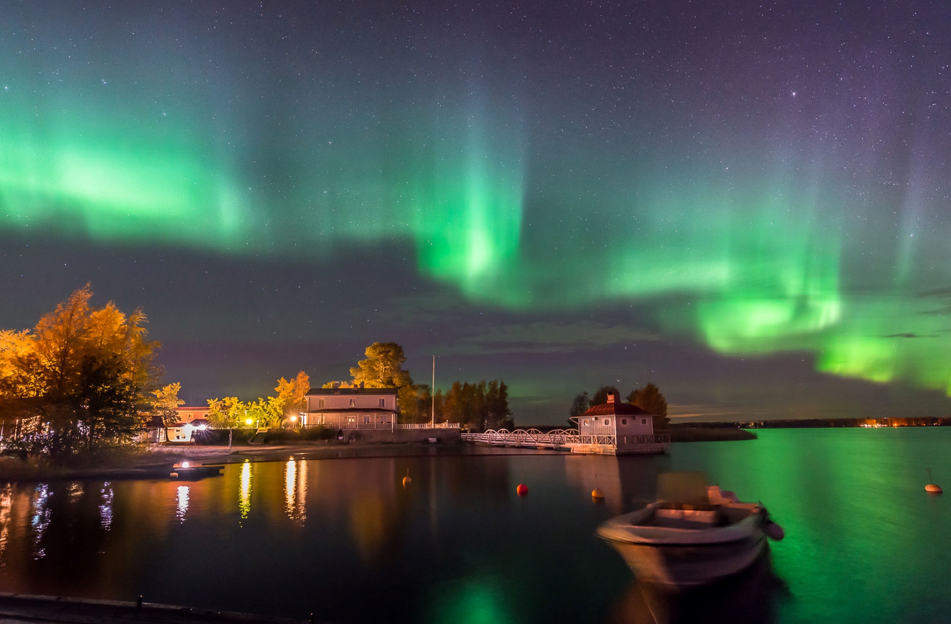 Kokkolan Villa Elba öisen revontulitaivaan alla. Kauniit vihreät revontulet, Aurora Borealis, valaisee meren vihreänä. Valot loistavat Nuorisokeskus Villa Elban pihassa ja merellä on yksi vene. Kuvaaja Hannu Moilanen.